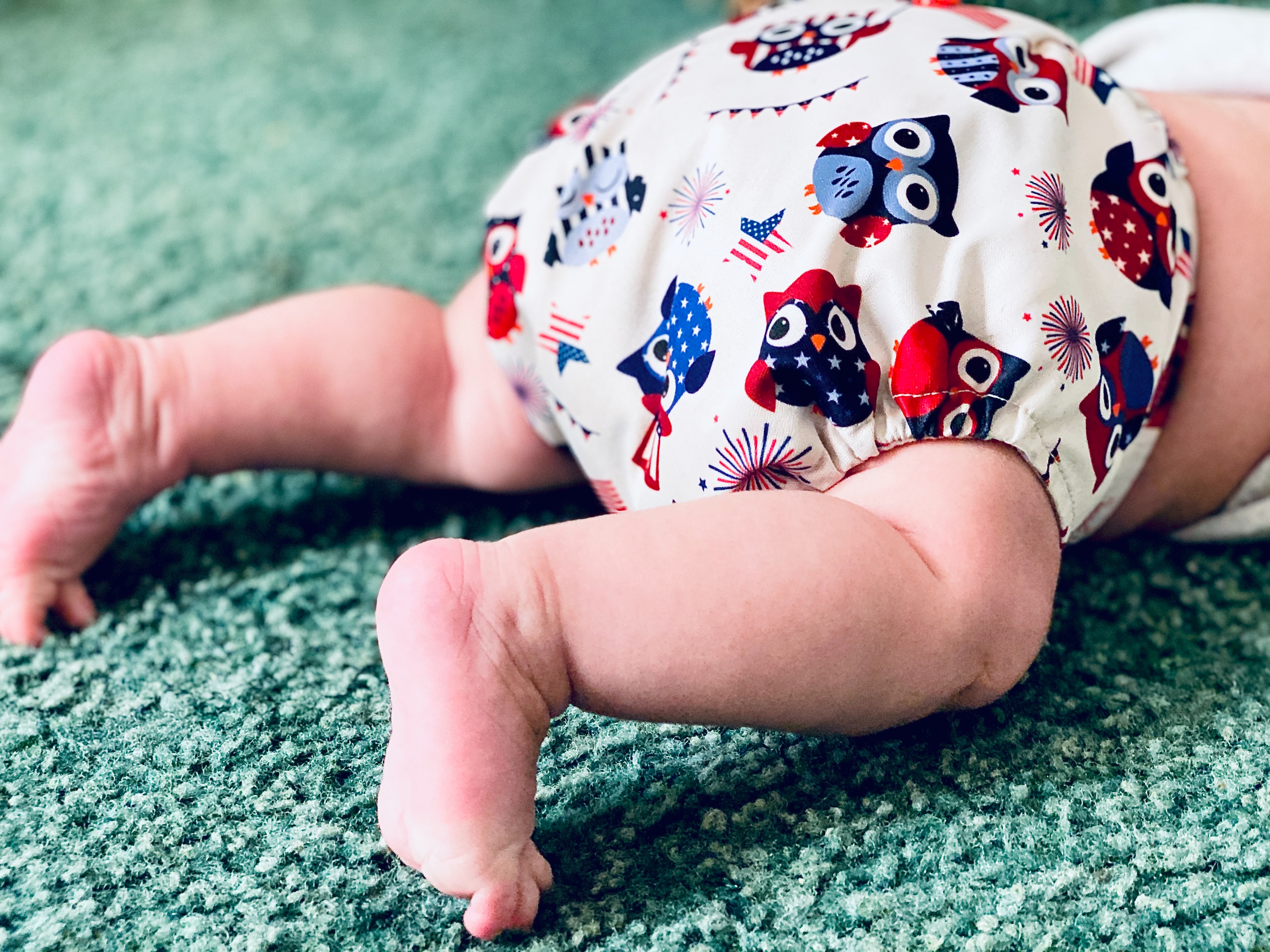 There\'s the bottom of a baby wearing a bulky, cloth diaper with an owl design.