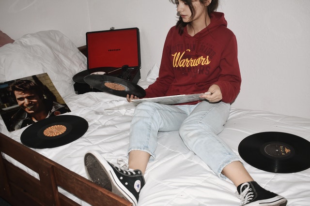 Girl sitting on a bed filled with vinyls and a record player