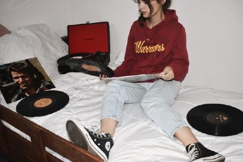 Girl sitting on a bed filled with vinyls and a record player Girl sitting on a bed filled with vinyls and a record player