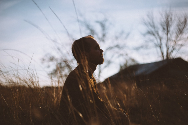 image silhouette of man sitting on grass field at daytime