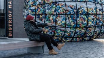 Man sitting in a bench with a structure full of plastic behind him