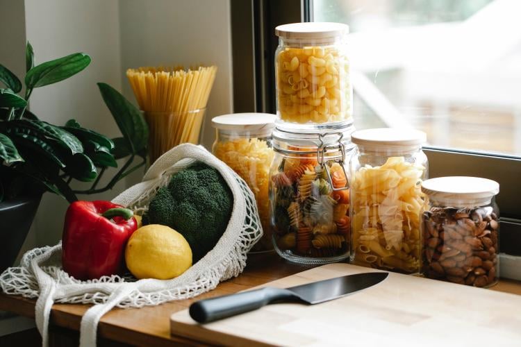 Food and containers There are glass containers filled with food. There\'s a wooden board with a knife on it, next to some vegetables.