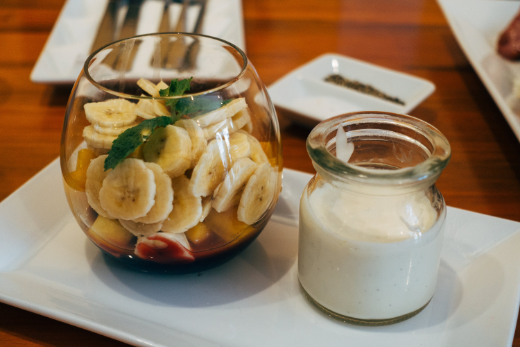bowl of mixed fruits next to a jar of kefir on a table
